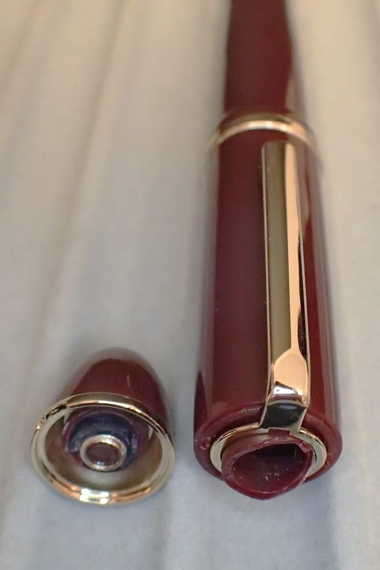 Broken cap of burgundy Jinhao X159 fountain pen, showing the top/finial sheared off on left, rest of cap on right