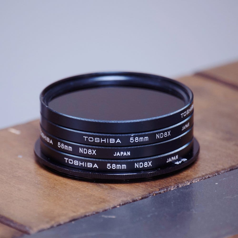 Close-up of a stack of 4 neutral density filters screwed together with a filter ring adapter