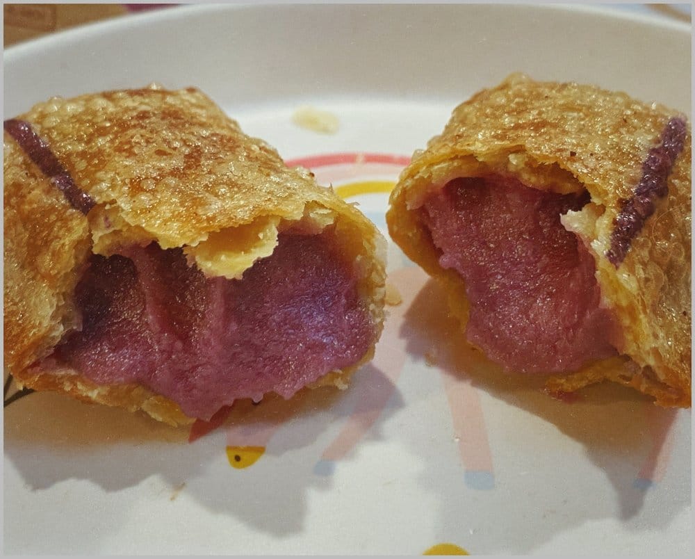 The crispy fried ube pie broken in half and plated up, showing its muted magenta ube filling