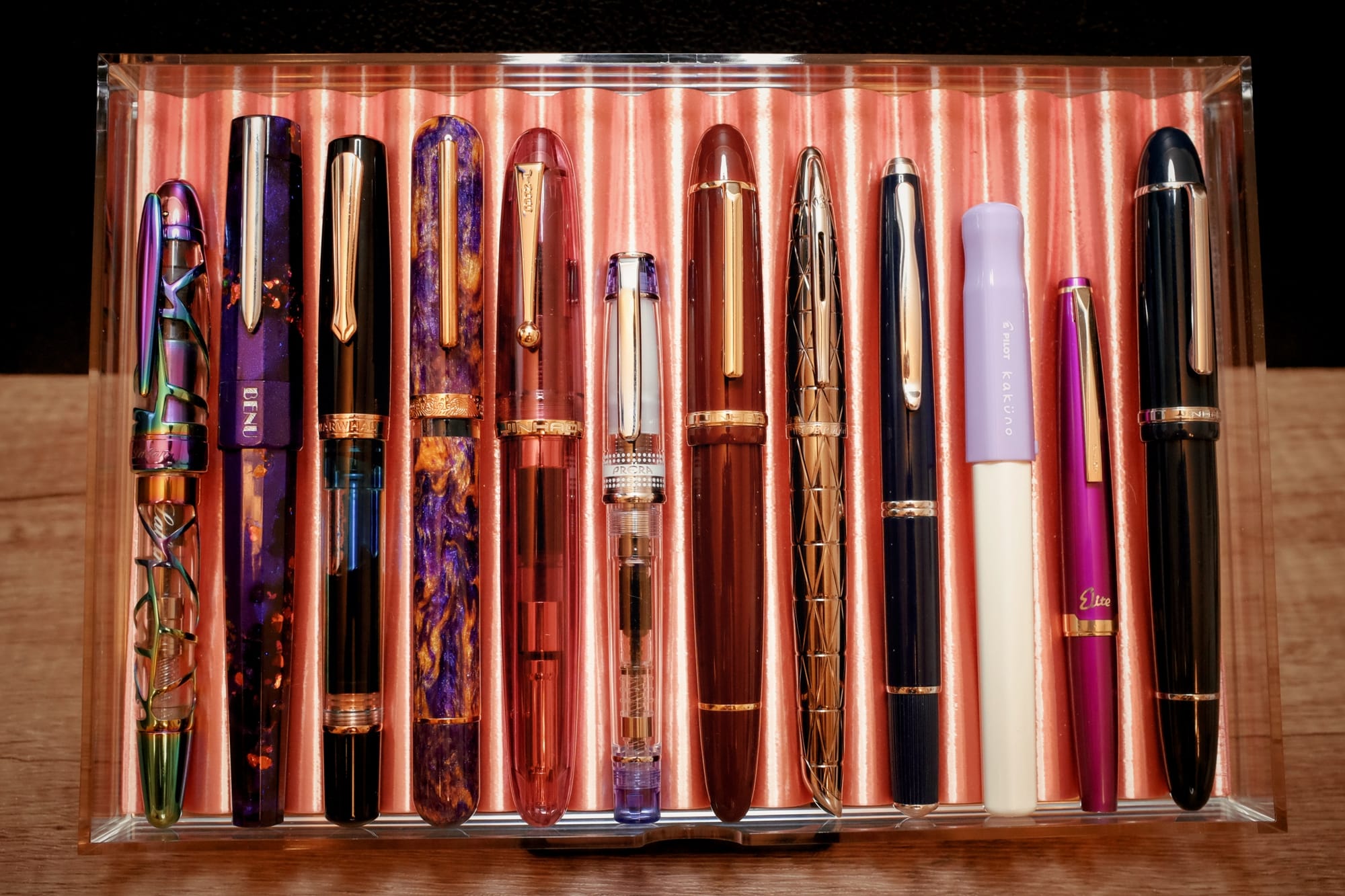 An acrylic drawer with a copper-colored 3D-printed tray holding 12 various fountain pens of different designs and sizes