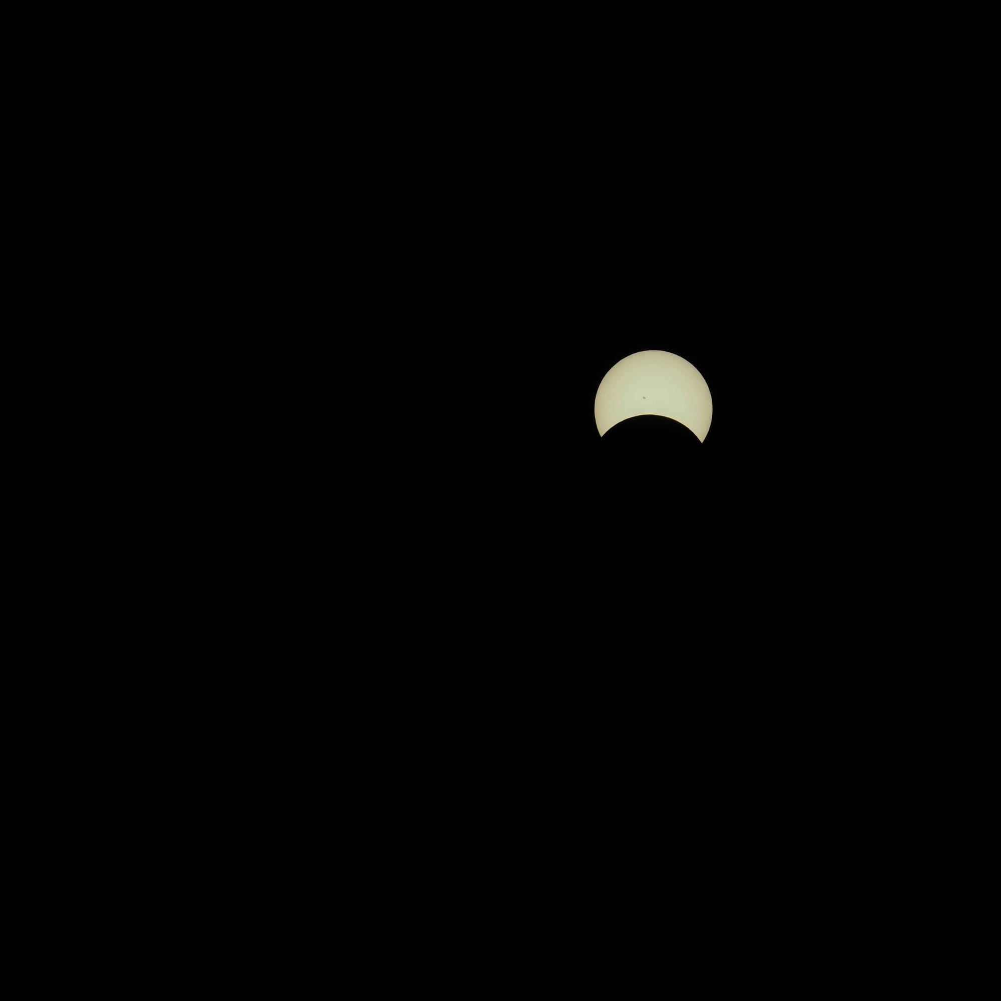 The eclipsed sun visible as a wide crescent shape against a black background, ~30% obscured