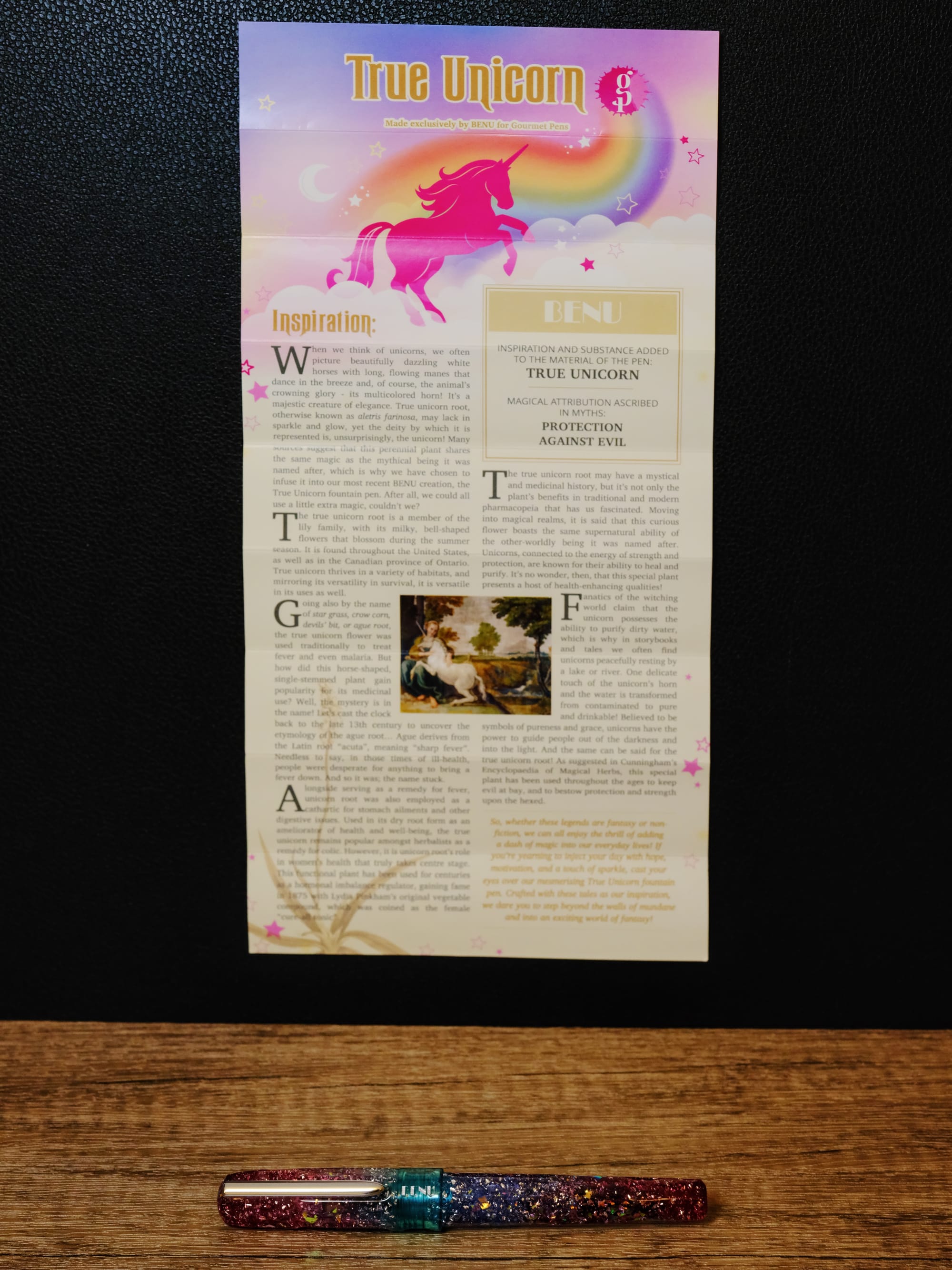 A text-heavy insert telling the story about the True Unicorn pen and its namesake root on a black background above the glittery, multicolored fountain pen sitting on a brown wood patterned surface