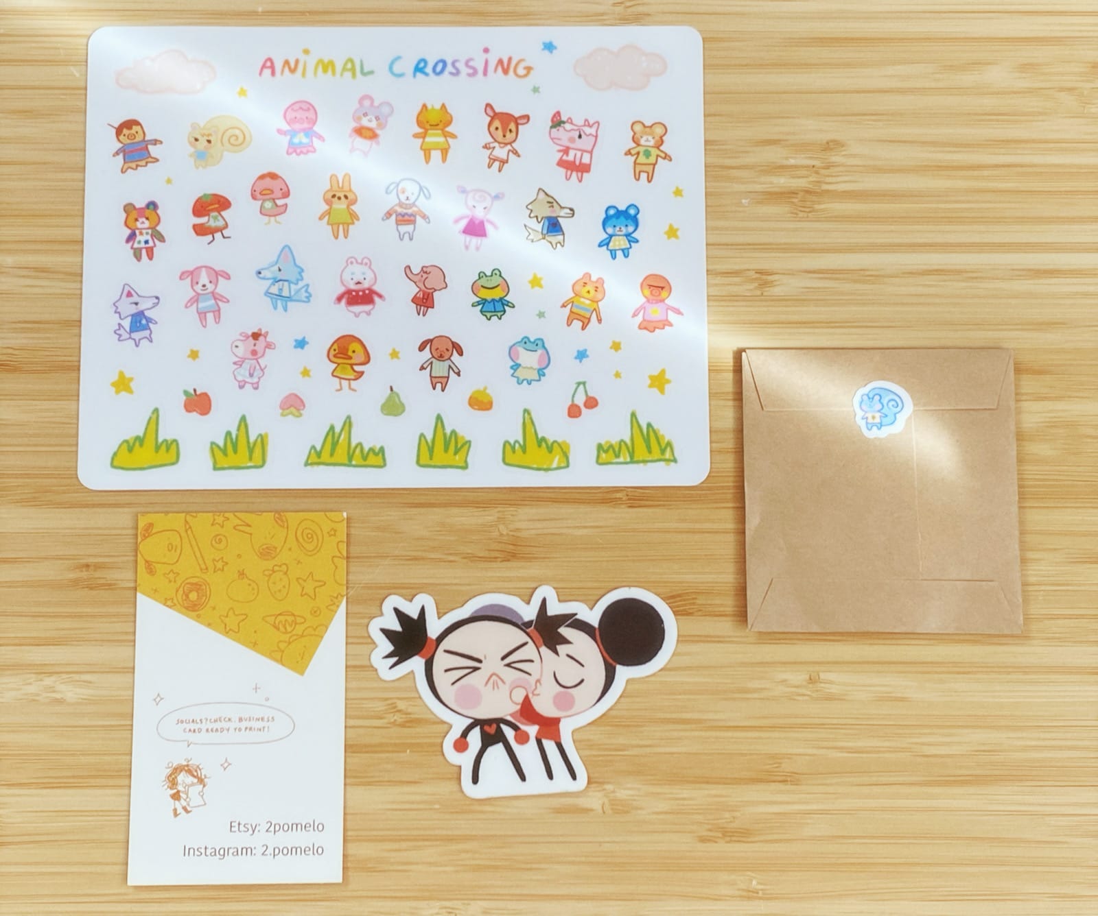 Animal Crossing sticker sheet with various animals from the game, a business card for the maker, 2 Pomelo, and a small brown envelope with a mystery batch of Animal Crossing stickers. 