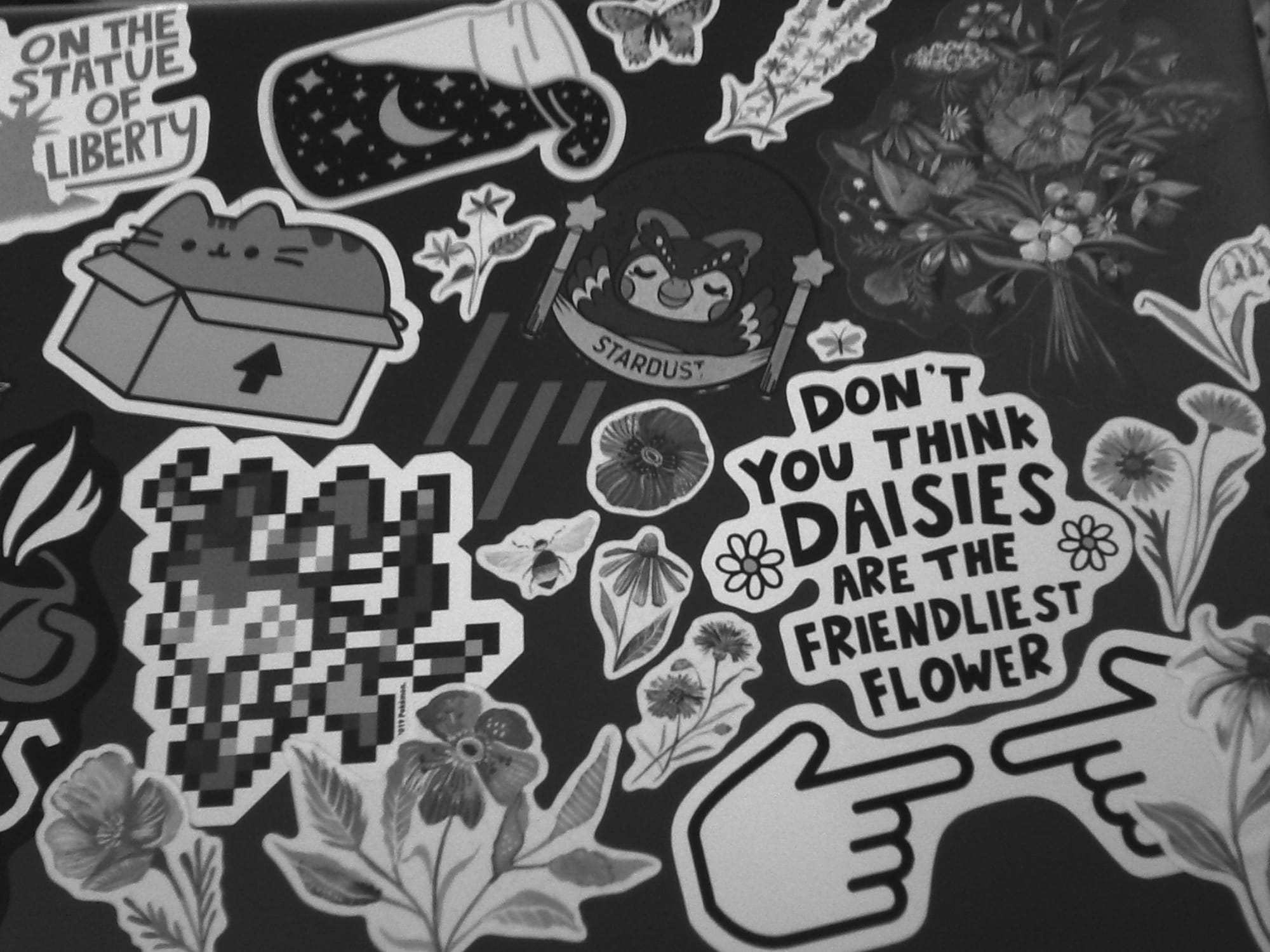 Slightly dim monochrome image of an HP laptop lid filled with various stickers of flowers, Pusheen, Celeste from Animal Crossing, etc.