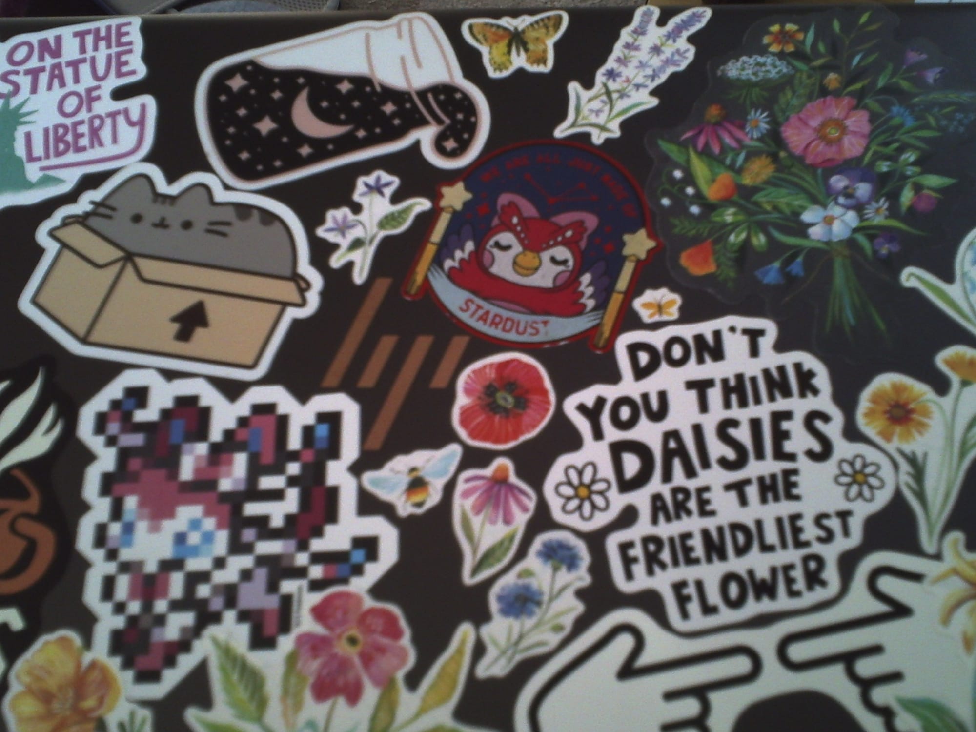 Slightly blurry and dim image of an HP laptop lid filled with various stickers of flowers, Pusheen, Celeste from Animal Crossing, etc.