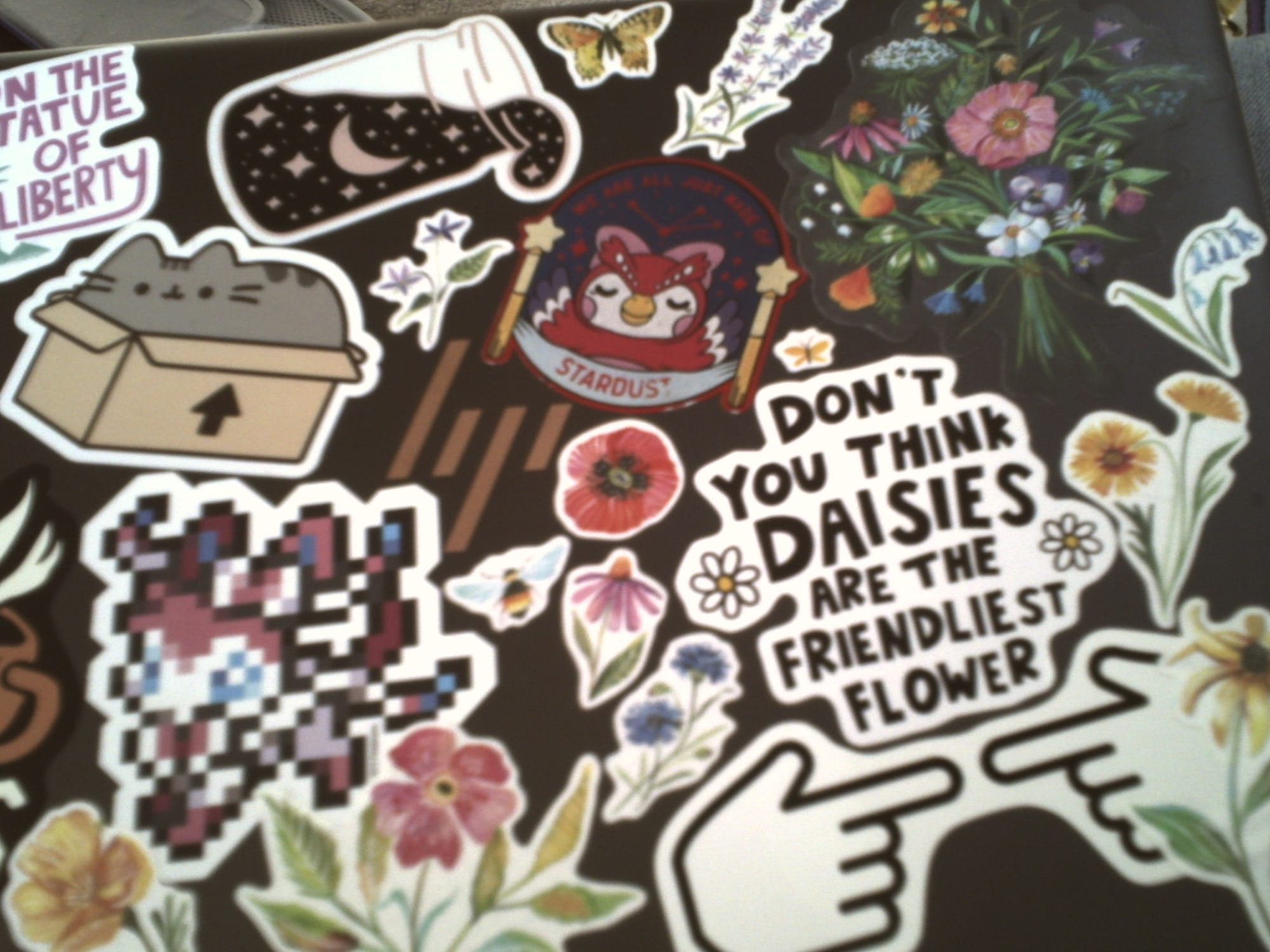 Slightly blurry and dim image of an HP laptop lid filled with various stickers of flowers, Pusheen, Celeste from Animal Crossing, etc.