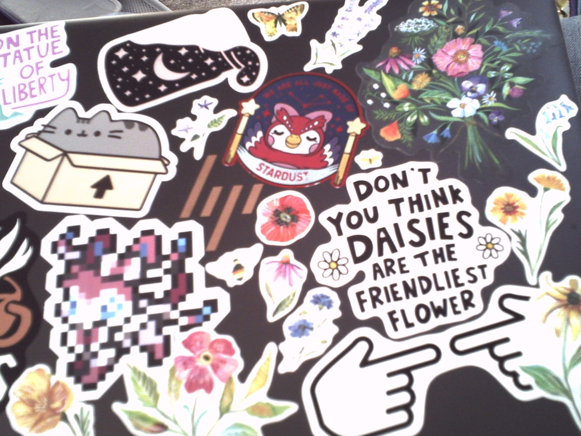 Slightly blurry image of an HP laptop lid filled with various stickers of flowers, Pusheen, Celeste from Animal Crossing, etc.