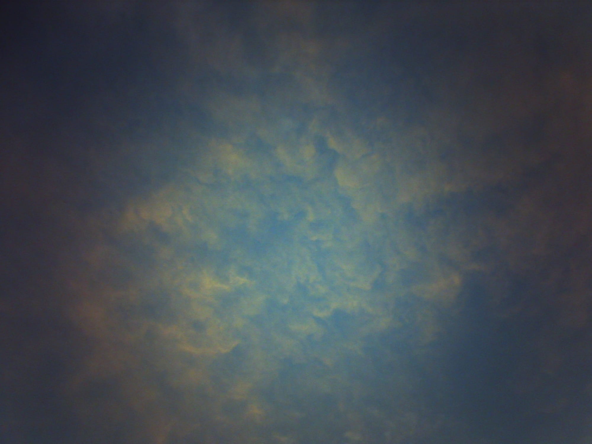 Lo-fi, grainy, strongly vignetted picture of a blanket of cotton candy clouds in a light blue sky