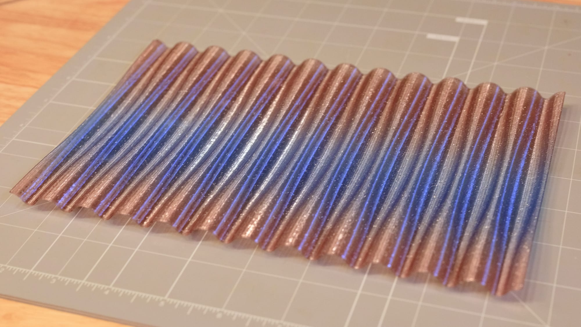 Angled view of a 3D-printed pen tray with a peach to blue to peach vertical gradient and glitter sitting on a gray cutting mat