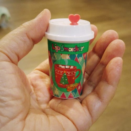 A hand holding a lip balm shaped like a disposable coffee cup with a pink heart-shaped plug for the sipping hole