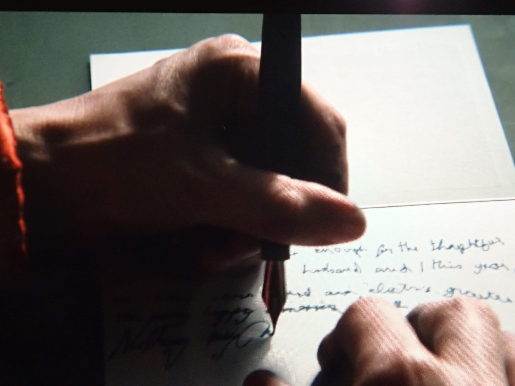 Screen capture of a left hand holding a fountain pen with the top of the nib facing the camera 