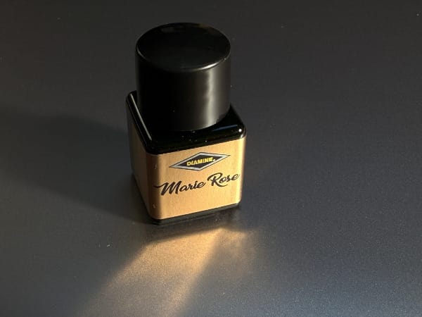 Close up of an Inkvent bottle showing off the bright gold label for Marie Rose ink, a gold reflection from the label visible