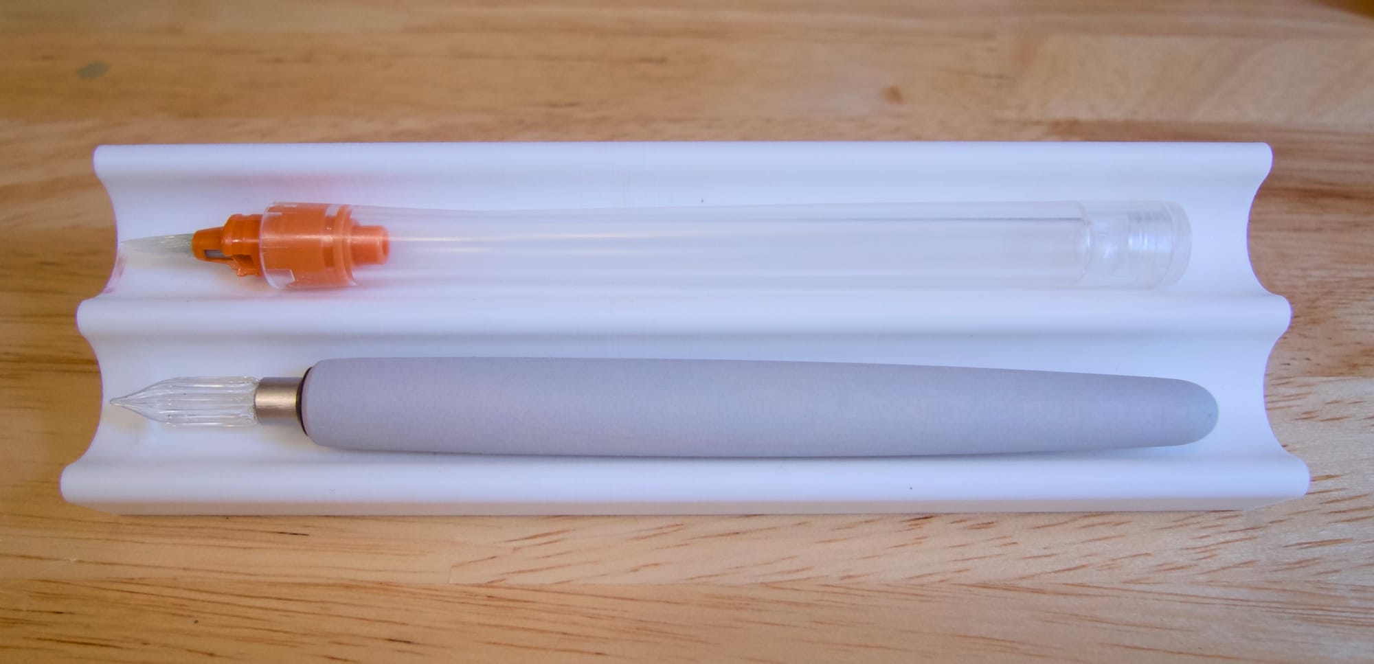 White 3D-printed pen tray with a brush nib in a clear pen body (top), and a glass nib in a short, gray nib holder (bottom)