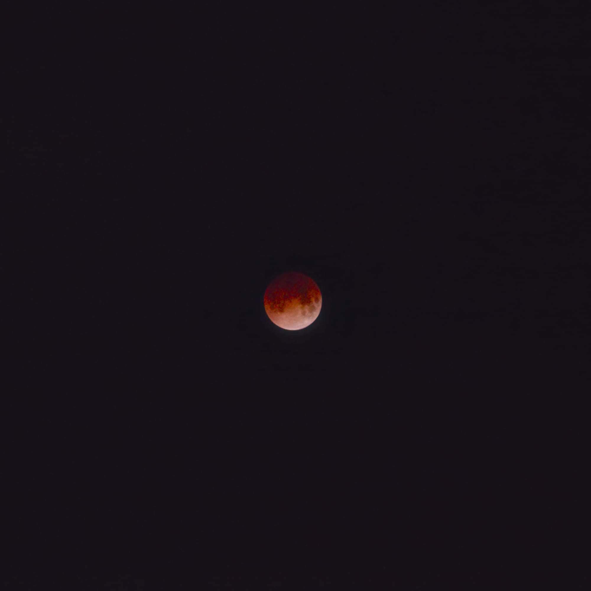 Square cropped image of black sky with a lunar eclipse in the center, already starting to transition out of peak