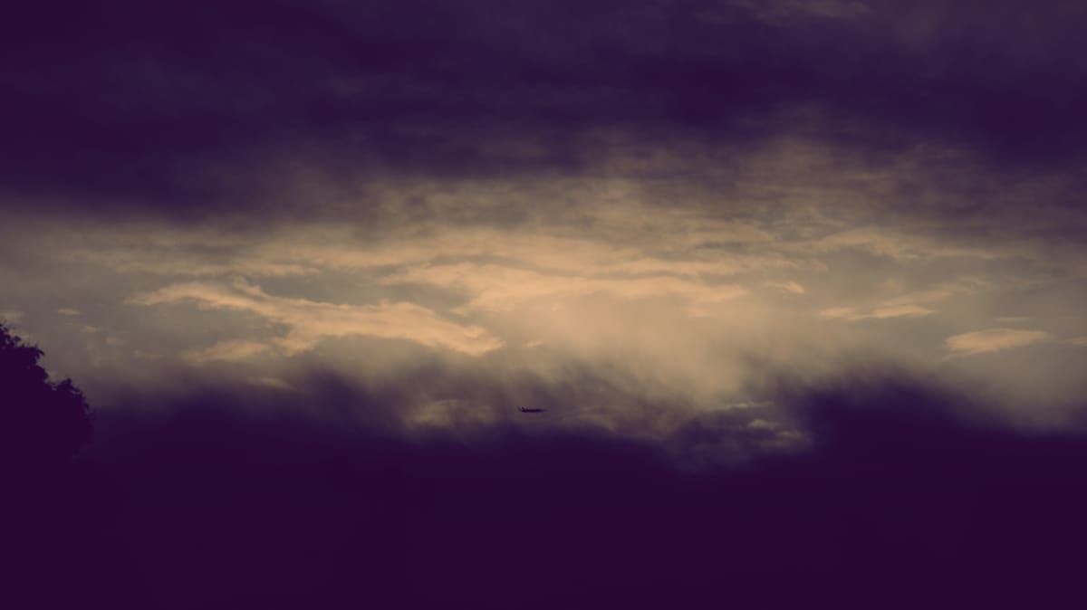 Dim sky with dark clouds on upper and lower edges of the frame, and a small plane visible through the lower dark clouds