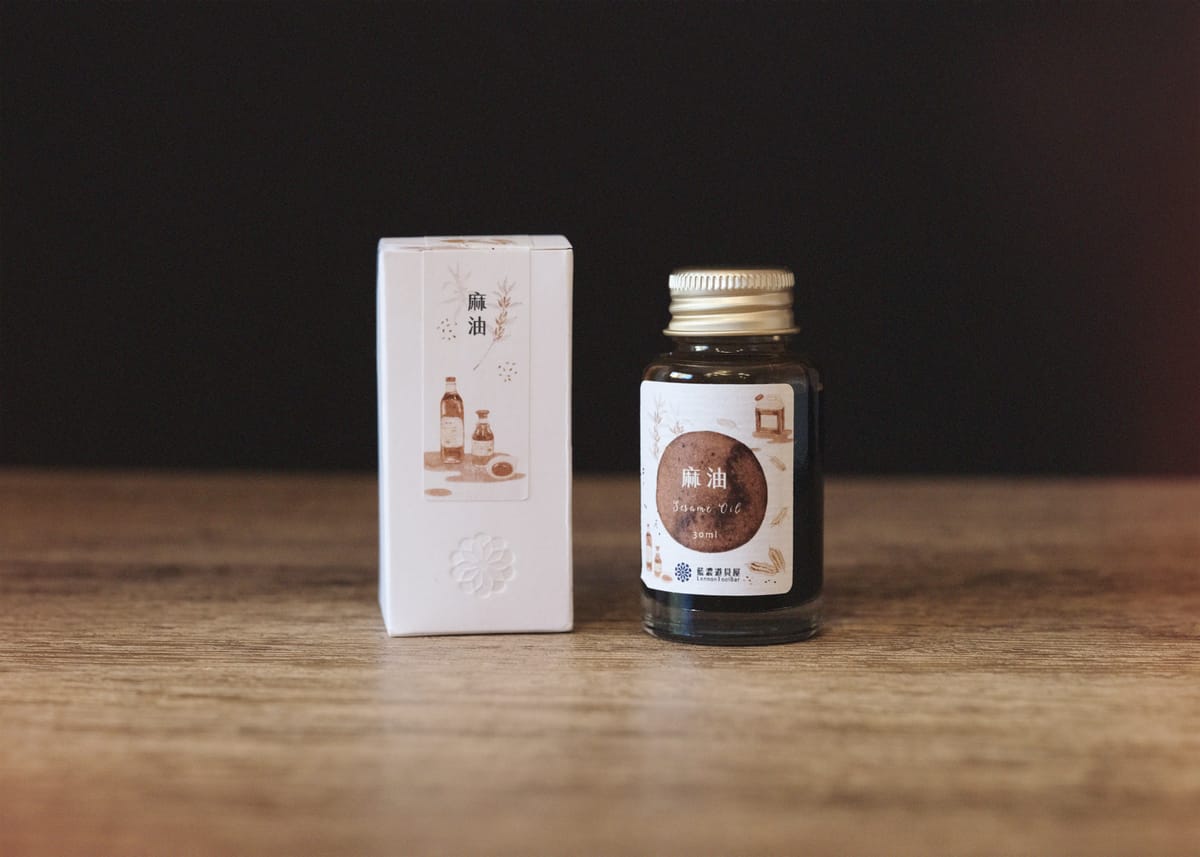 Bottle of Lennon Tool Bar's Sesame Oil ink next to its minimal product box against a black and wood pattern background