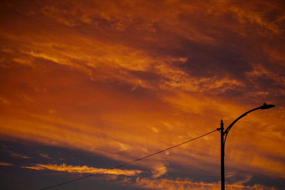 Vivid sunset sky with dramatic clouds, gradient of red-orange to dark blue-black, light post in bottom right corner