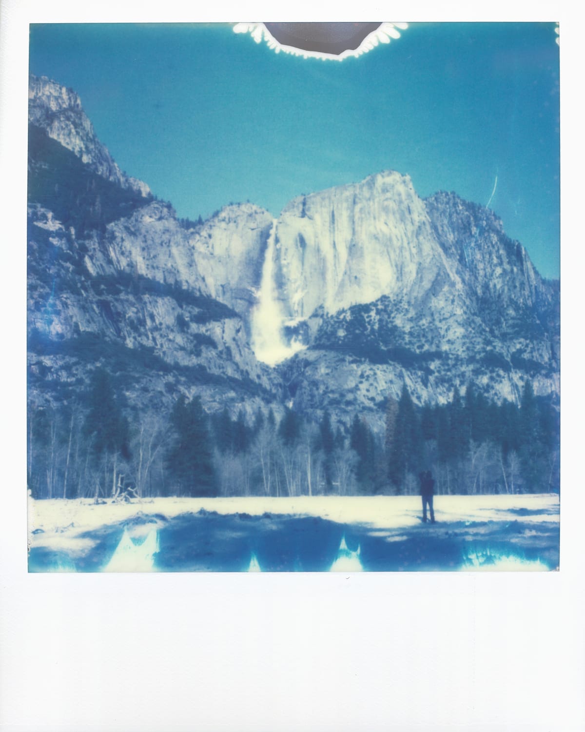 Scan of an Impossible Project film photo taken at Yosemite showing a waterfall in winter, a person below taking a picture