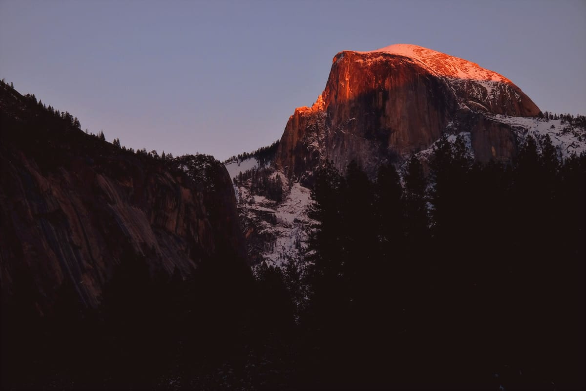 Telephoto picture of Half Dome in Yosemite, a crescent of red sunlight across its peak, the rest in dark shadow