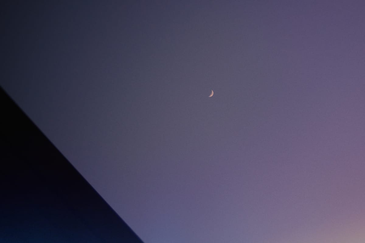 Very small crescent moon near the middle of the frame, with a black triangle in the lower left corner