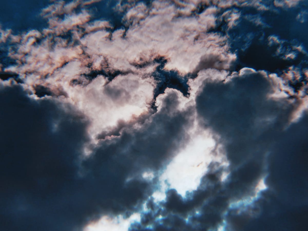 Clouds in a deep blue sky with dramatic lighting, and some iridescent highlighting around some clouds at the top of the frame