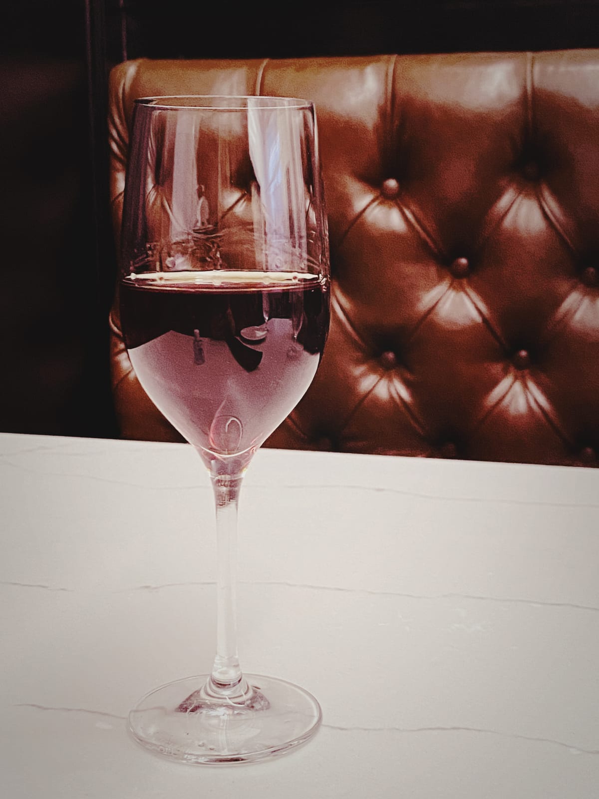 A small glass of tawny port on a white “marble” table in front of a tufted “leather” chair back
