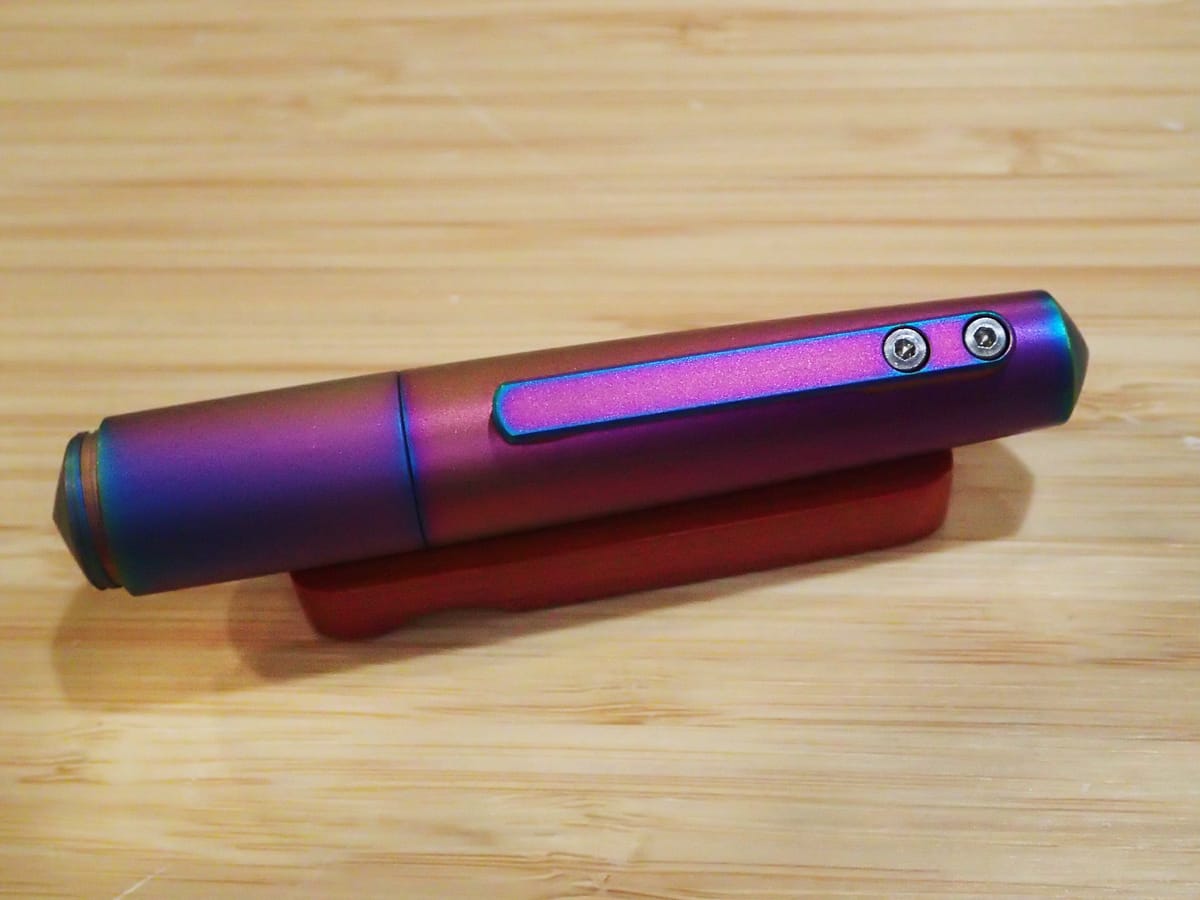 Titanium pocket pen, not much longer than the pen rest it’s sitting on, anodized with rainbow colors