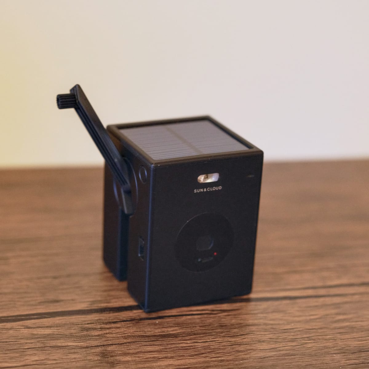 A black cube-shaped camera with its hand crank extended, and its solar panel on the top face showing