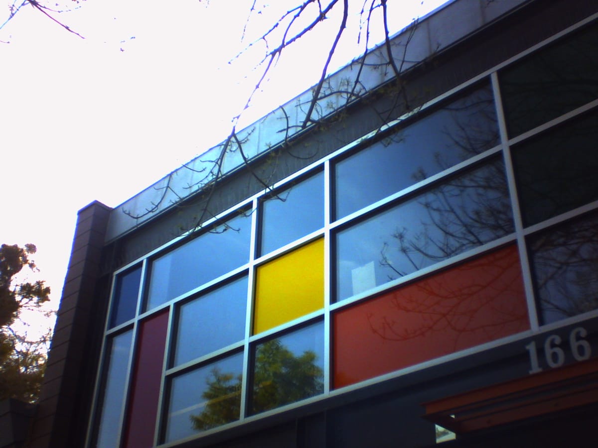 Low-res picture of a building facade with a colorful front window reminiscent of a Mondrian painting