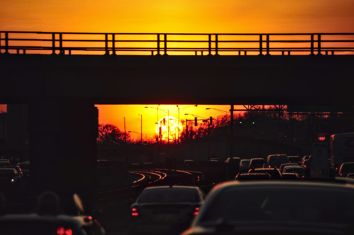 Heavy traffic traveling under and overpass leaving Chicago, the sun blazing on the horizon at sunset, sky deep orange