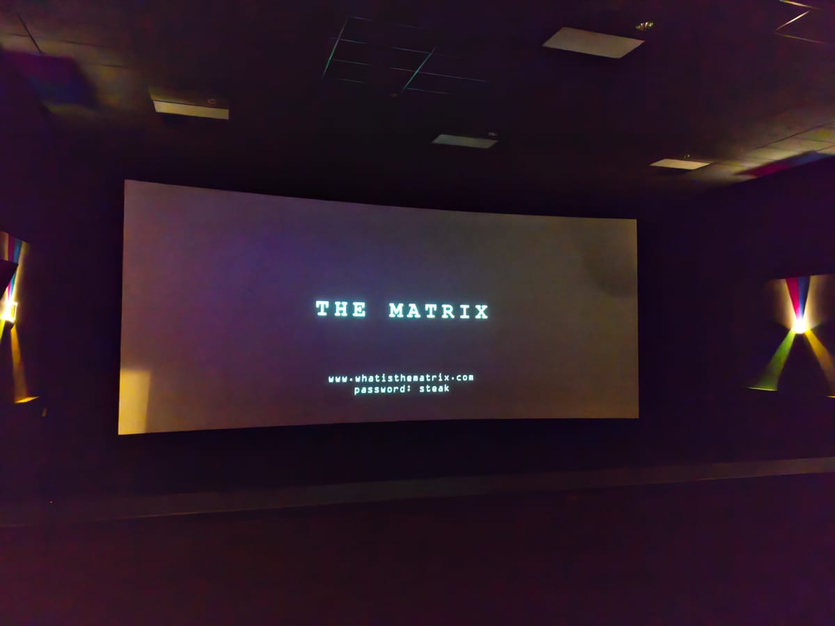 Movie theatre screen showing "The Matrix" and "www.whatisthematrix.com, password: steak"