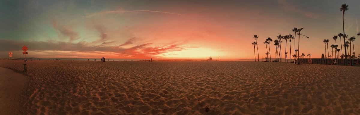 Panoramic view of Venice Beach at sunset, palm trees in far background on right, partial walking path on left