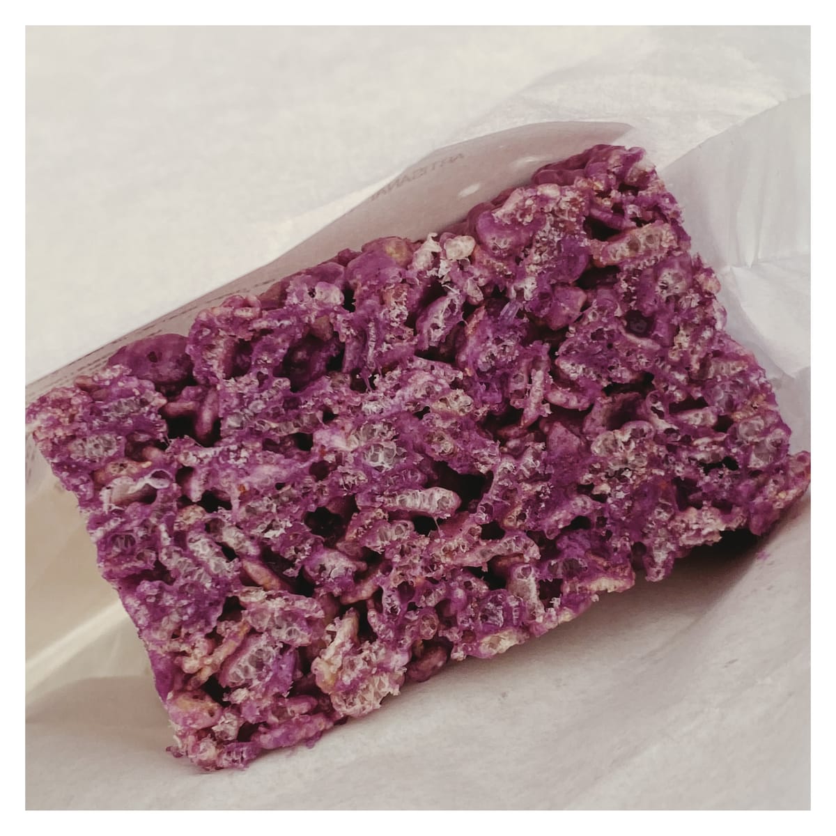 A purple rice crispy bar inside a white paper bag