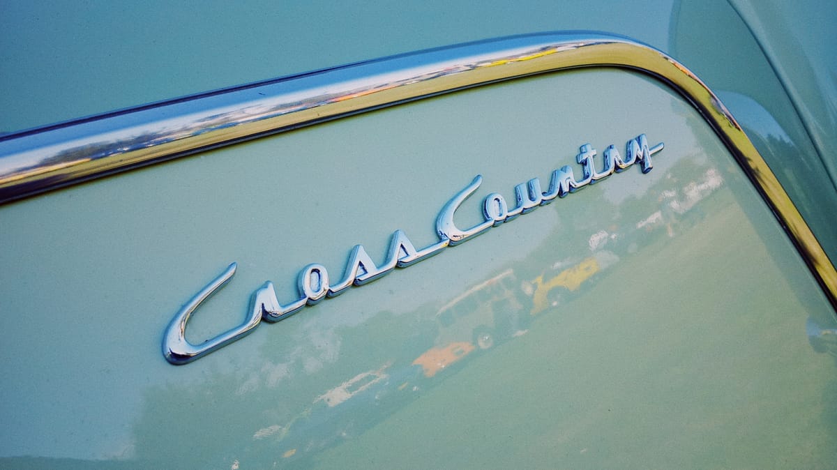 Close up of a vintage chrome logo on an old pastel green car that says "CrossCountry" in a kind of script font