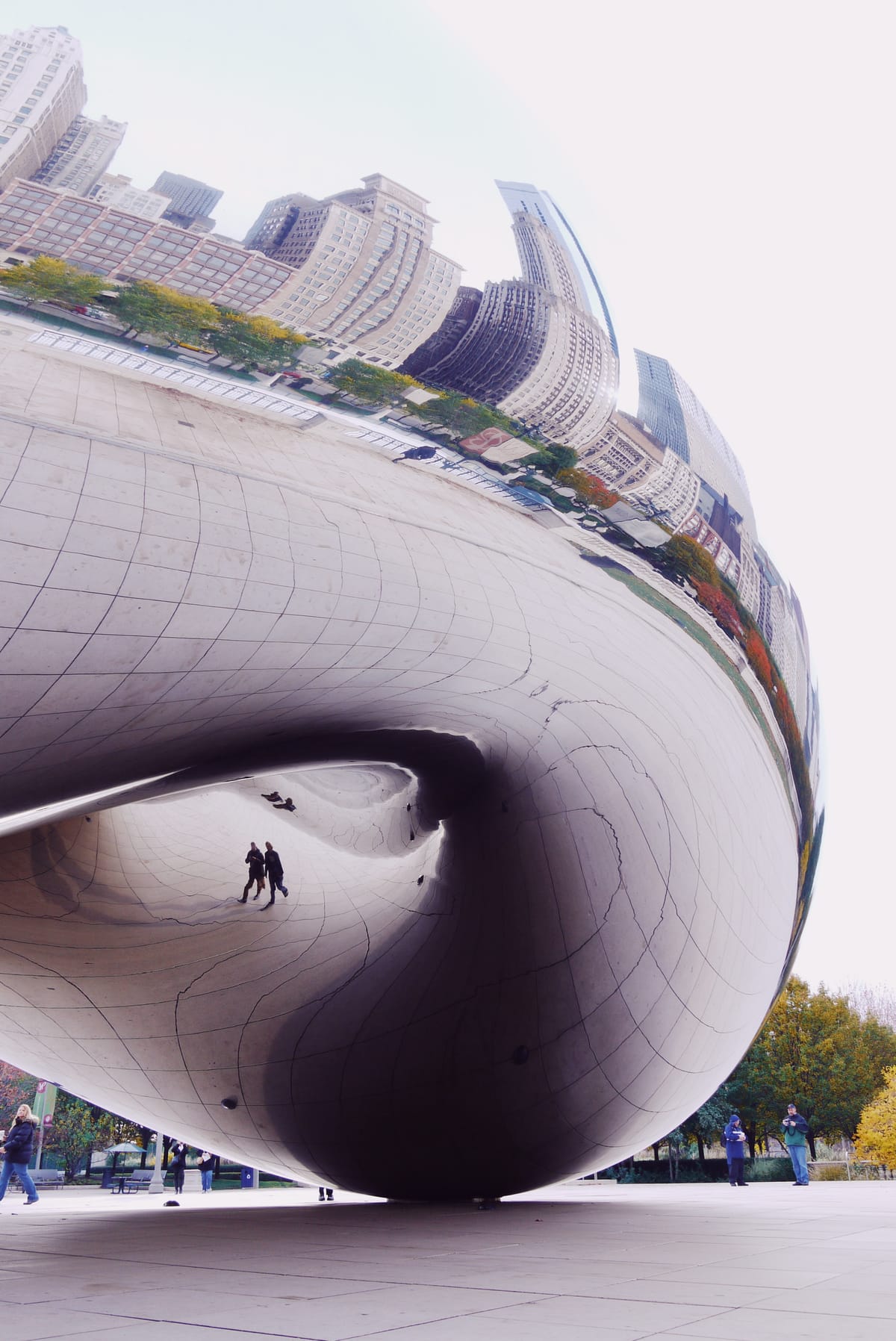 The Cloud Gate metal sculpture with its outer surface reflecting Chicago skyline, underside reflecting two passersby