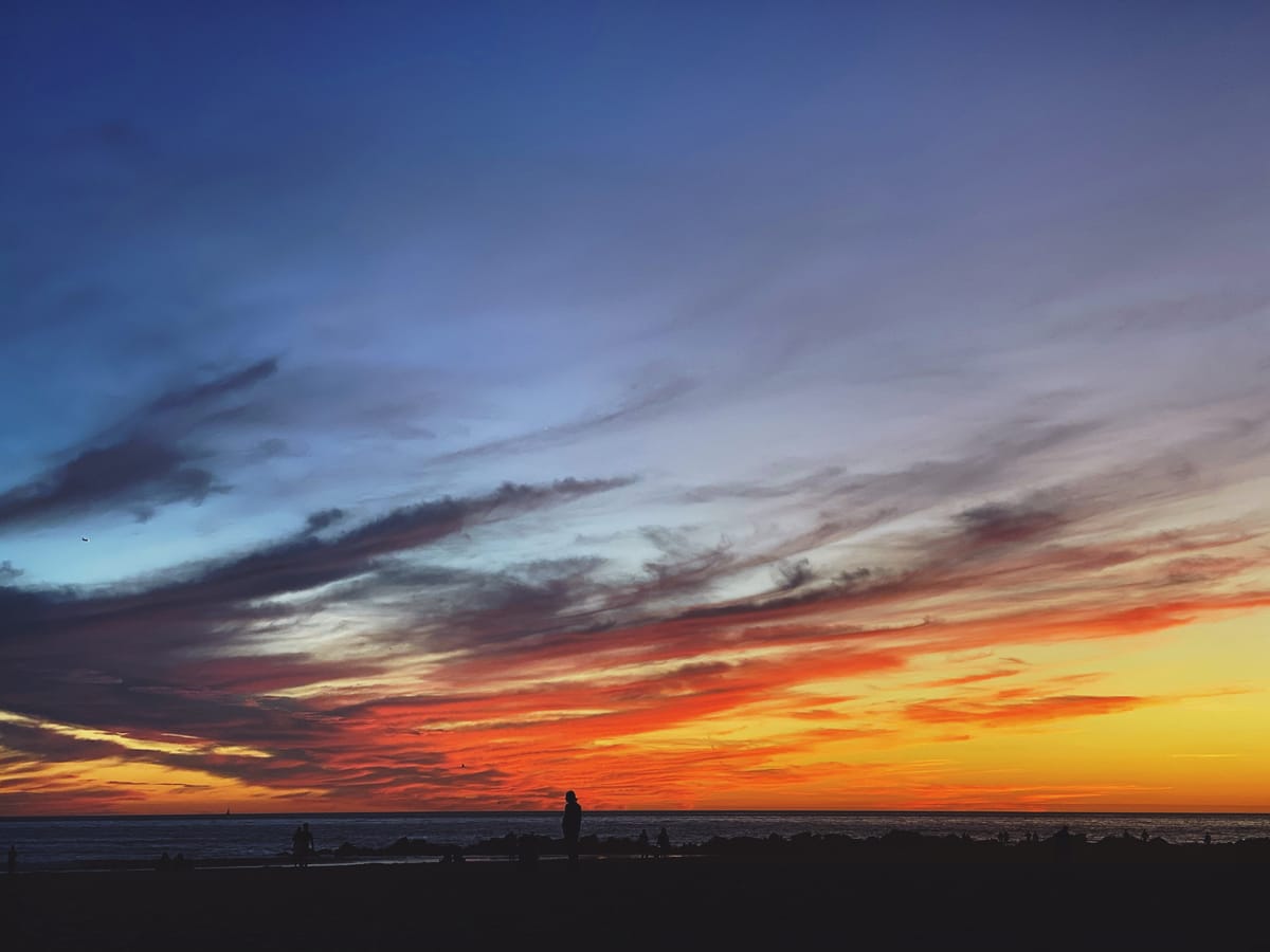 Vivid sunset at the beach with wispy dark clouds across the blue and orange sky, silhouettes of people walking past