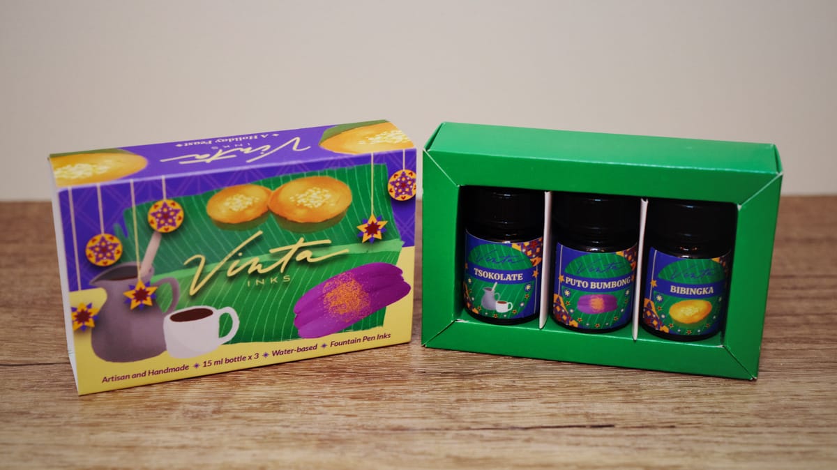 Open green box containing 3 ink bottles, with the outer sleeve displayed to the left of the box, with holiday art