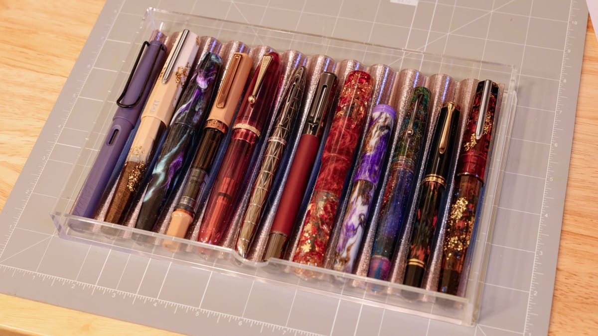 Angled view of a 3d-printed pen tray in an acrylic drawer, housing 12 different fountain pens