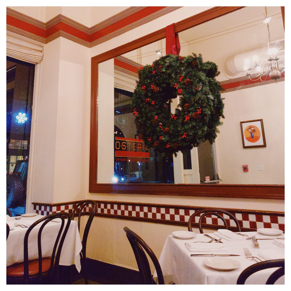 View of the Osteria name in the mirror, partially obscured by a large evergreen holiday wreath with red berries