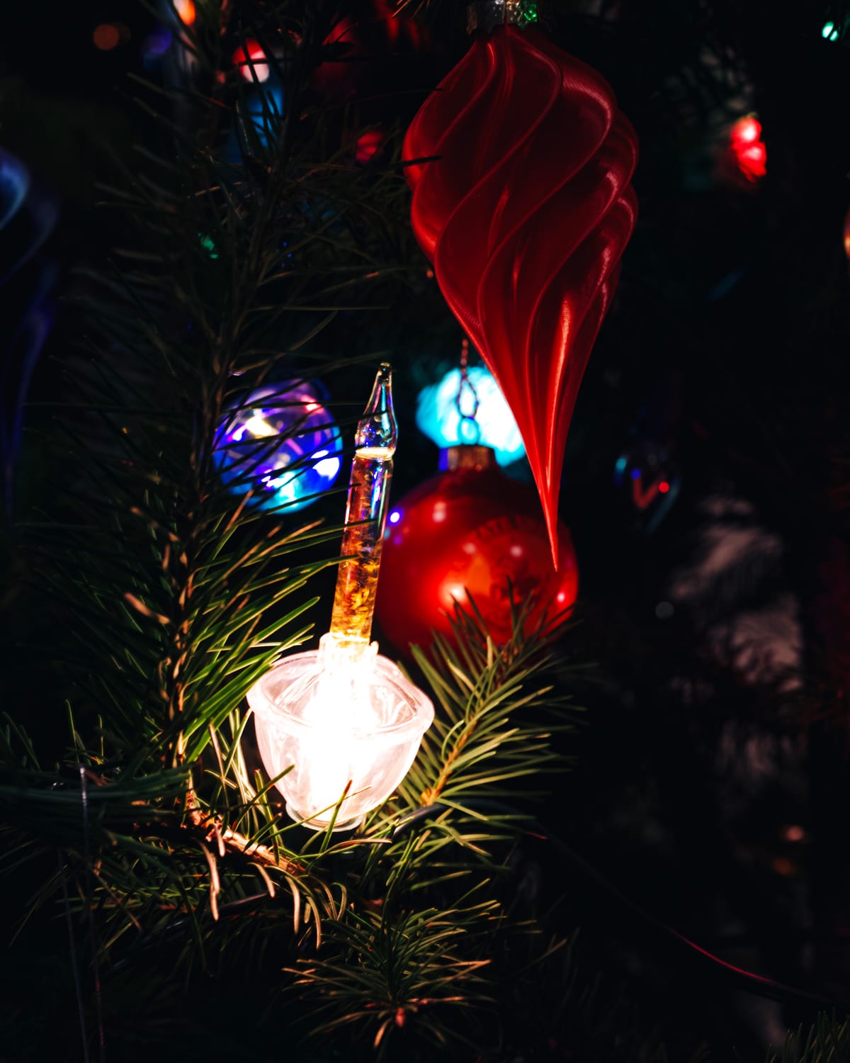 Close up of a lit "bubble light" ornament, its liquid agitating with gold glitter, other colorful ornaments in background