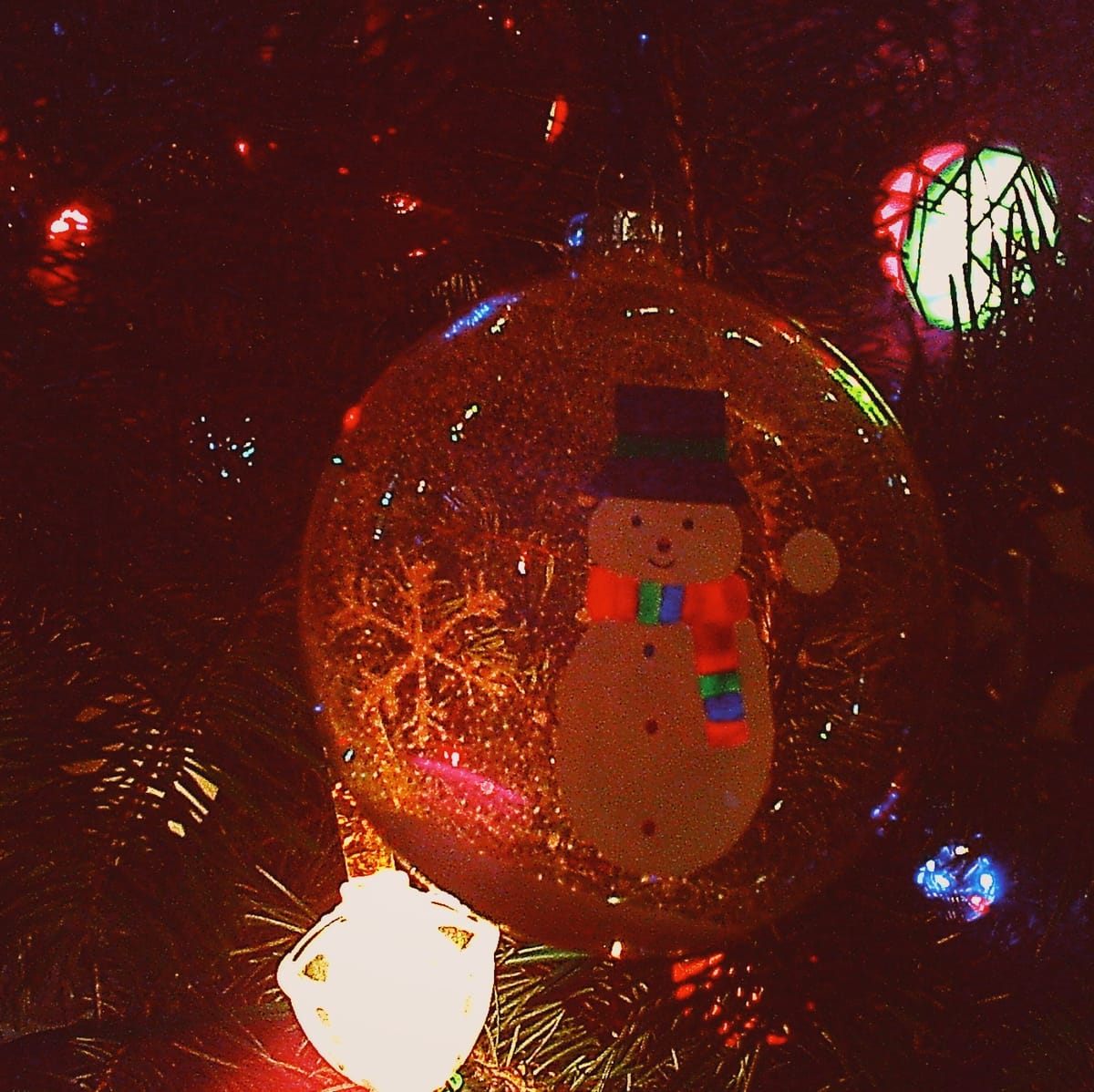 Grainy close-up of a transparent glass ornament on which a snowman is painted, two very bright bubble lights flanking it