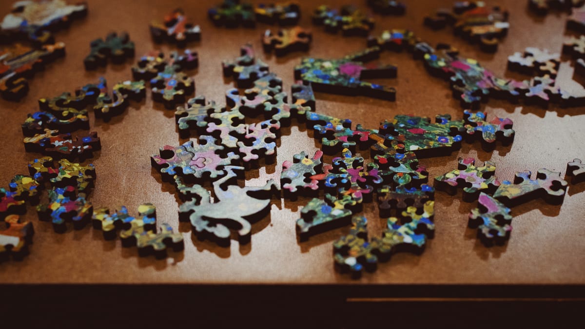 Scattered puzzle pieces on a particle board tabletop, viewed at an overhead angle