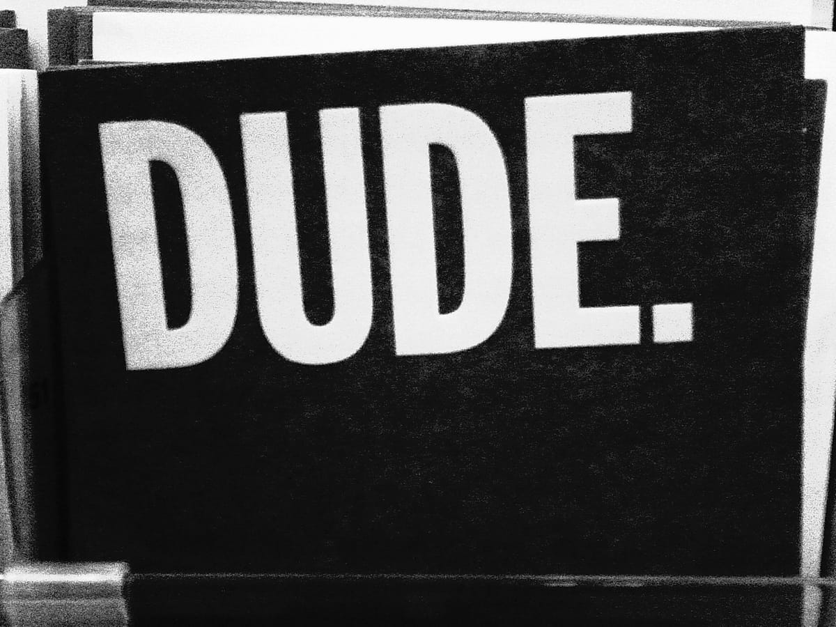 Black and white picture of a card with a black background and large, all capital letters in white that say, "DUDE."