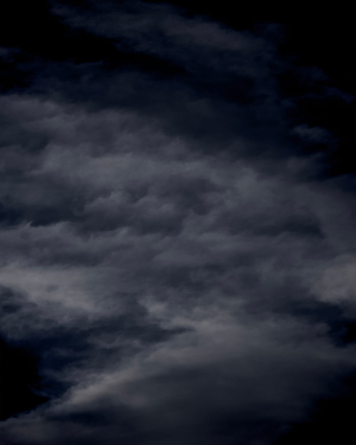 Almost monochrome, telephoto picture of gray cottony and wispy clouds against a very dark blue sky