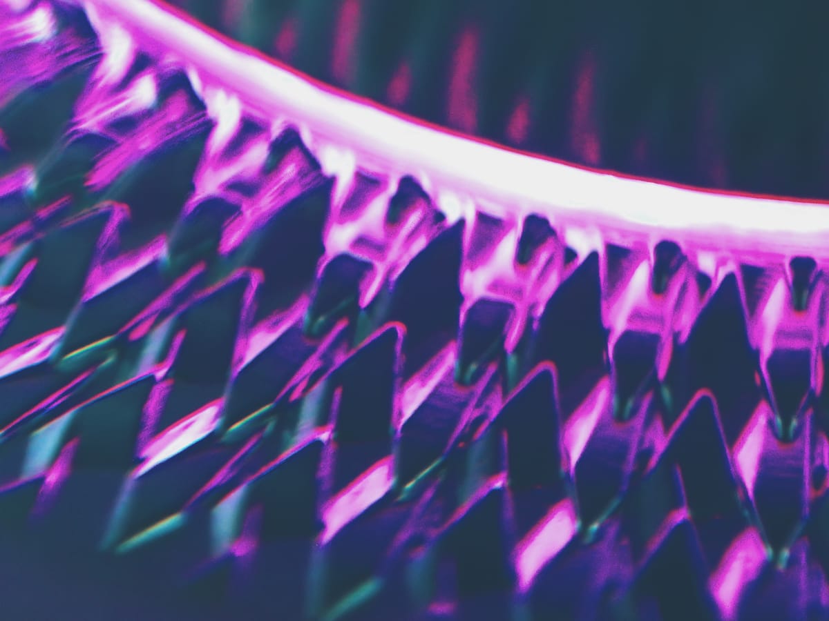 Abstract macro of backlit, repeating rows of diamond shapes, lit in magenta and blue-green tones