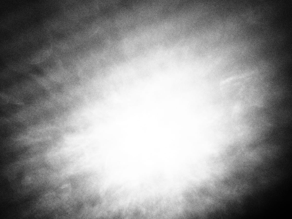 Abstract black and white image of a bright spot punching through the middle of a dark, textured area