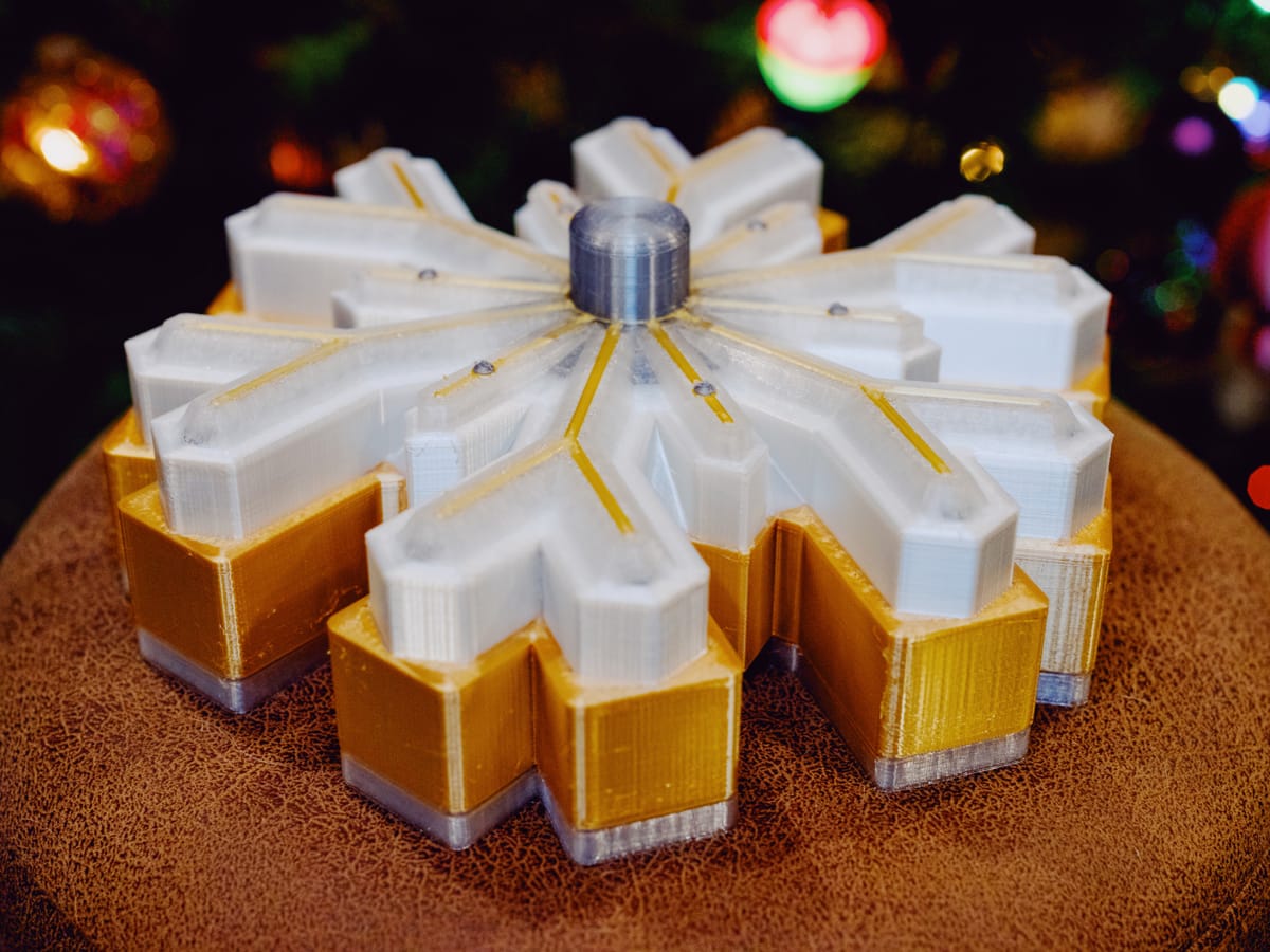 A 3D-printed, snowflake-shaped box made of gold, white, clear, and silver filament