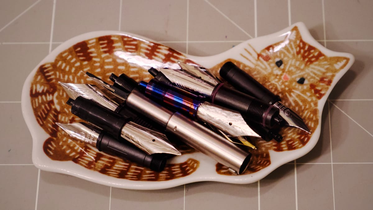 Cat-shaped ceramic dish holding a pile of different fountain pen nib units