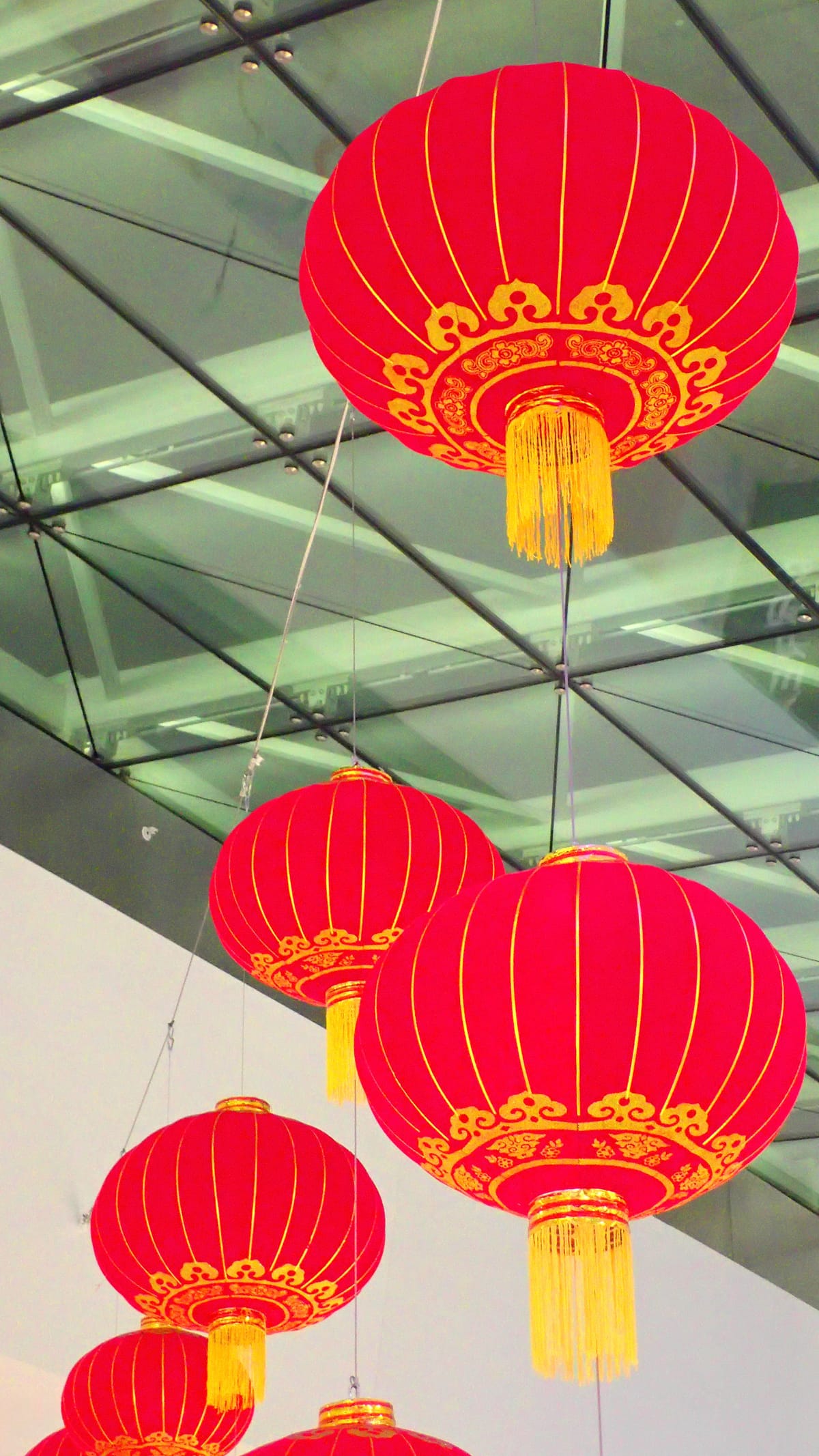 Oversaturated picture of red and gold Asian lanterns for lunar year celebration, with greenish glass panel roof in background