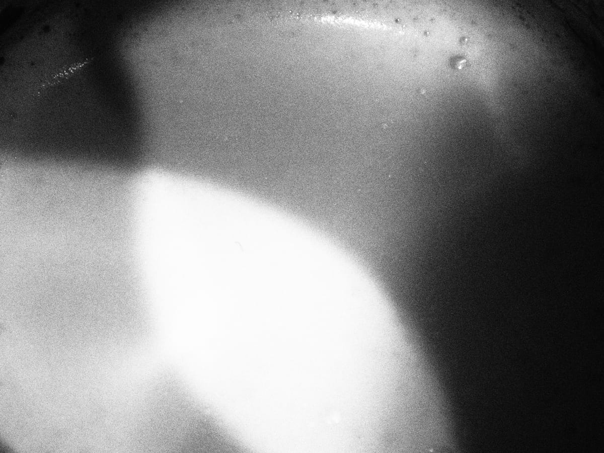 Grainy black and white abstract image of milk foam in a latte with 3 tones of lighting, a bright oblong spot in middle